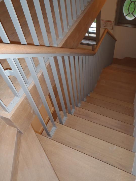 Trapleuning met lichtgrijze spijlen bij een houten trap